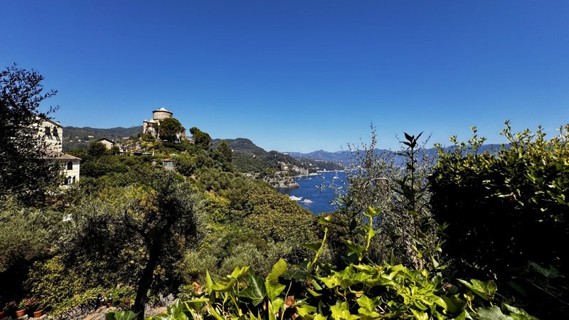 A coastal hillside with a stone tower overlooking boats on blue water